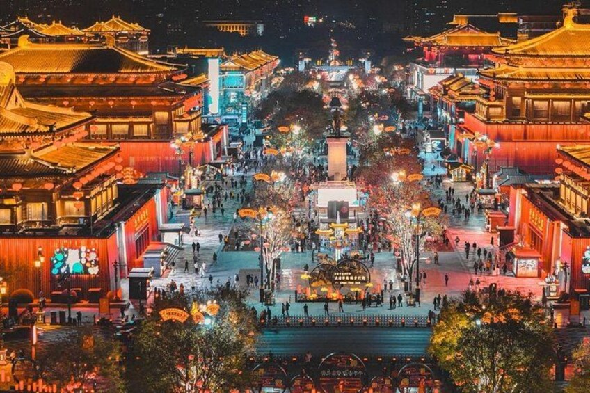 Una calle tradicional china iluminada de noche, con edificios brillantes y una plaza central. 5