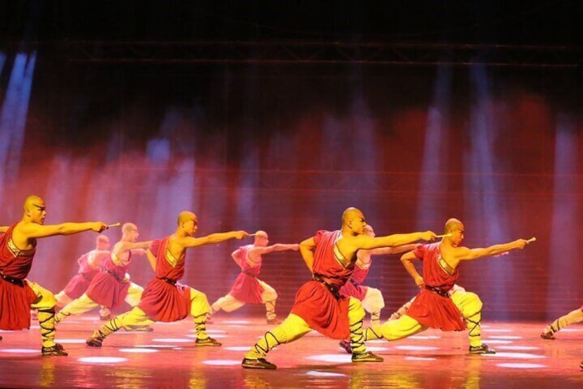 Un grupo de bailarines vestidos con trajes rojos y amarillos actúan en un escenario iluminado por focos. 2
