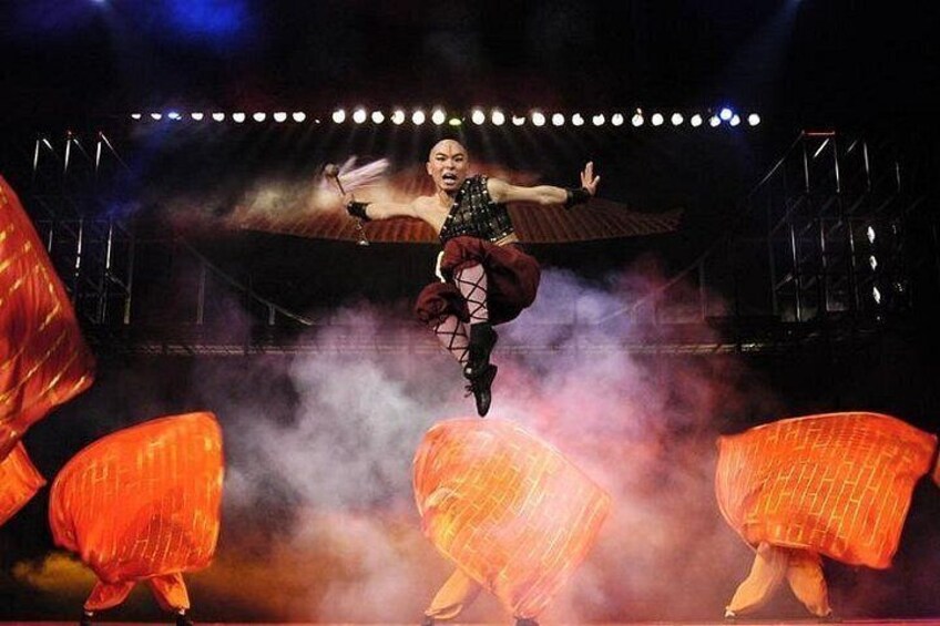 A performer in mid-air with large orange props on stage. 2