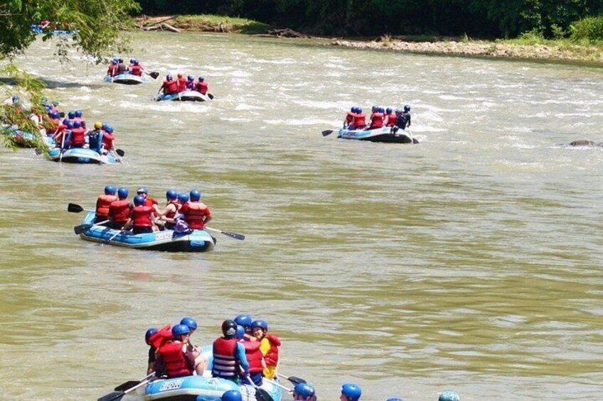 Multiple white water rafts with people wearing red life jackets and helmets. 2