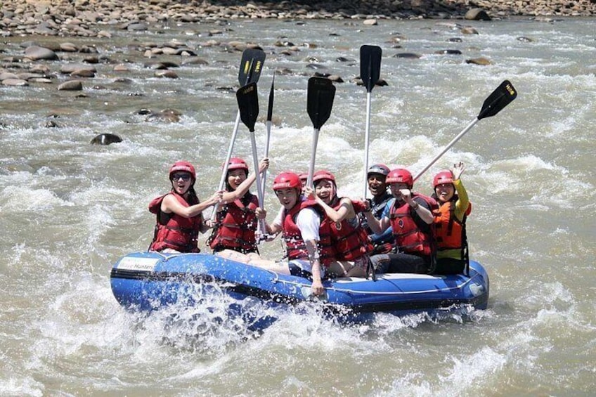 A group of people in a blue raft on a river, wearing life jackets and helmets. 4
