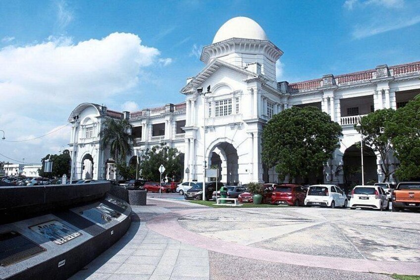 A large white building with a dome and arches, surrounded by parked cars and trees. 3
