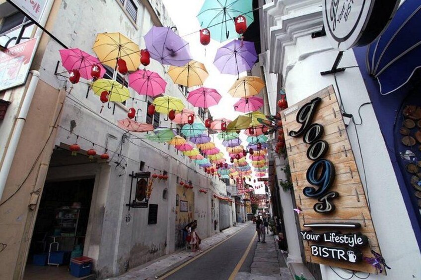 A street with colorful umbrellas hanging overhead, a wooden sign with 'JoJo's' and 'Your Lifestyle BISTRO' text, and a narrow alleyway. 4