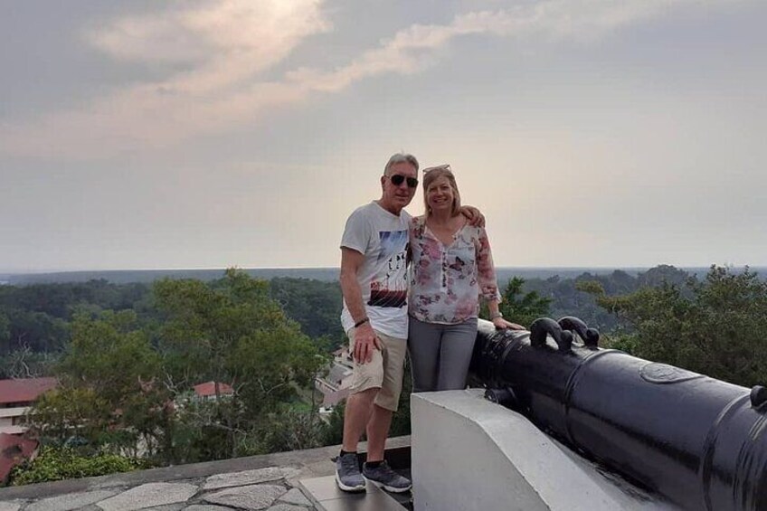 Two people standing on a stone platform with a cannon in the foreground and a view of a forested landscape in the background. 2