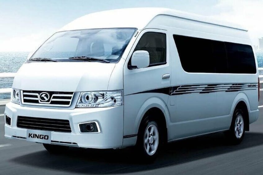 A white KINGO van driving on a road with a body of water in the background. 2