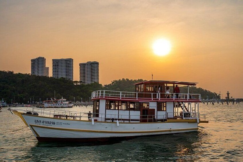 A boat with a cabin and passengers, docked at sunset with buildings in the background. 4