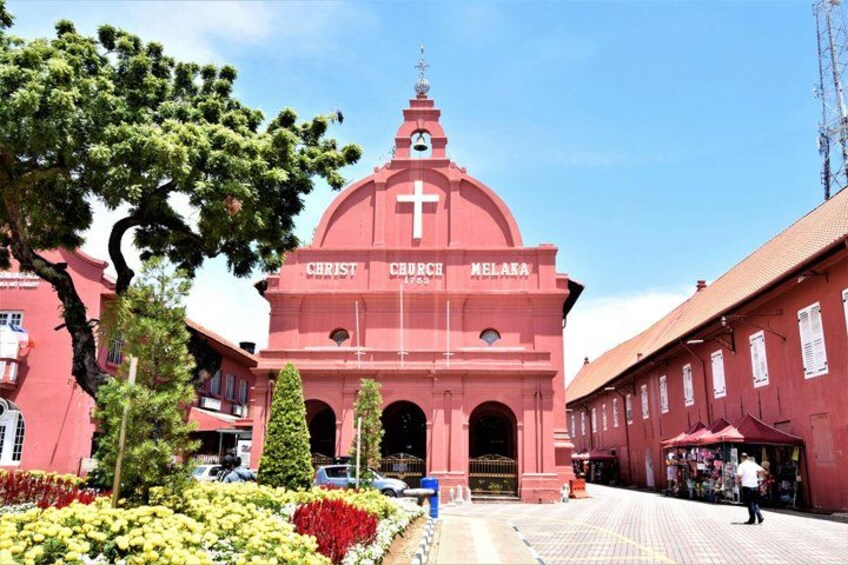 A red church with a cross on top, surrounded by trees and flowers. 5