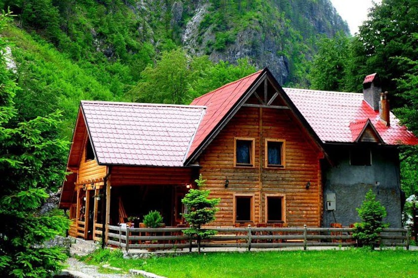 Une cabane en rondins de bois, avec un toit rouge, entourée d’une végétation luxuriante et avec des montagnes en arrière-plan. 5