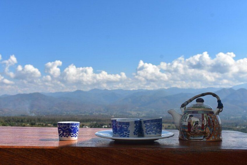 A teapot and cups on a table with a mountainous landscape in the background. 2