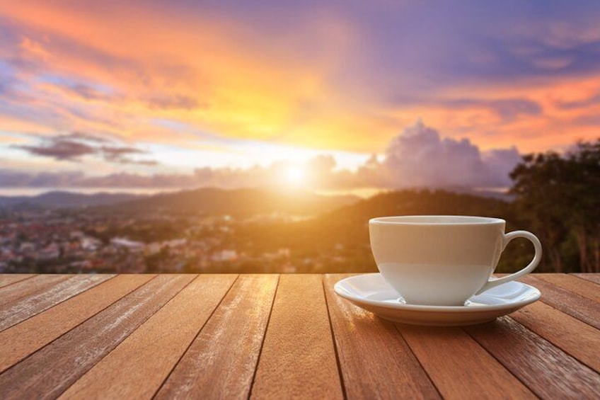 Une tasse blanche posée sur une table en bois, avec un coucher de soleil en arrière-plan. 2