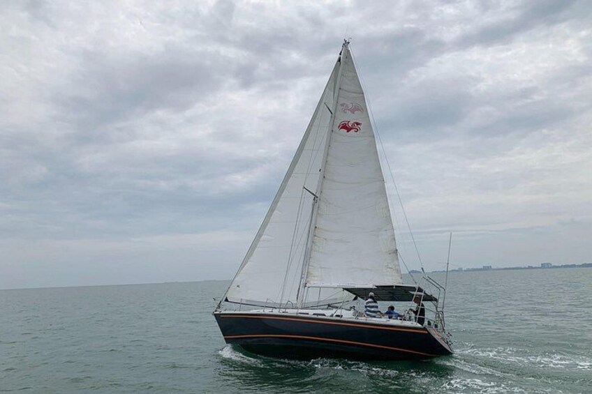 Un voilier à voile blanche, arborant un logo rouge sur le mât, navigue sur une eau calme. 3