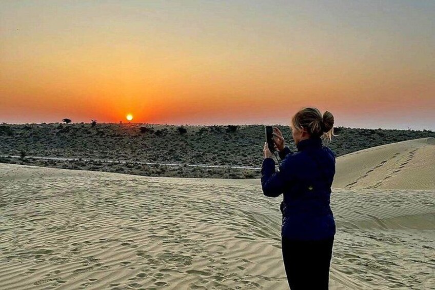 A person taking a photo of the sunset over a desert landscape. 1