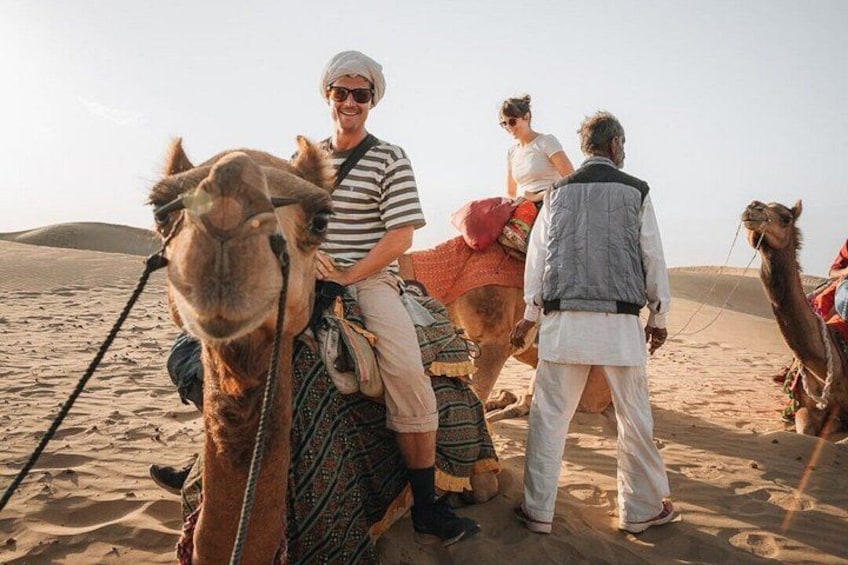A desert landscape with people riding camels. 5