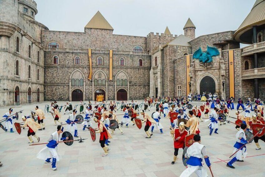 A medieval reenactment in a courtyard with stone buildings and a large blue dragon sculpture. 2