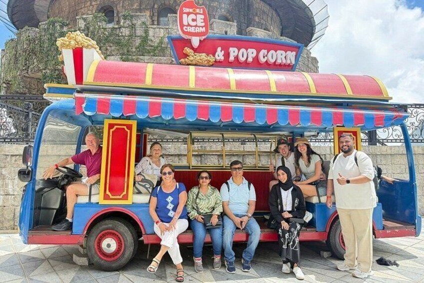Un grupo de personas sentadas y de pie junto a un carrito colorido de helados y palomitas de maíz. 2
