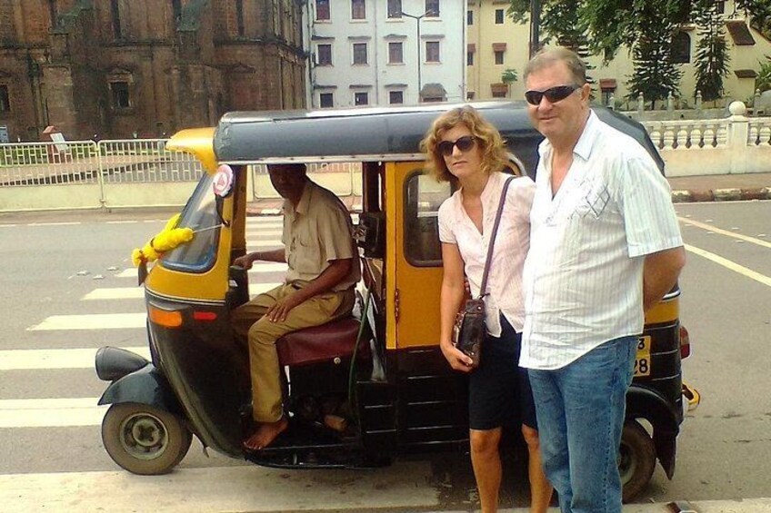 A man and a woman standing next to a yellow auto-rickshaw on a city street. 2