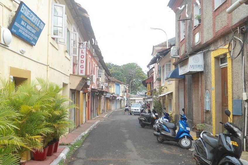 A narrow street lined with colorful buildings, parked scooters, and a sign for a lodge. 3