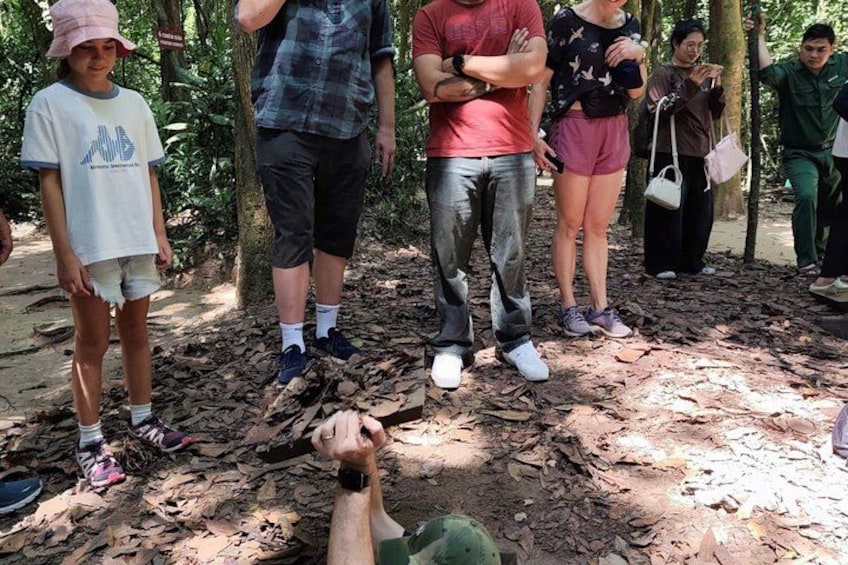 A group of people standing in a forested area with leaf-covered ground. 5