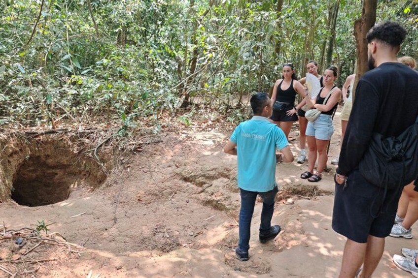 Un gruppo di persone in piedi attorno a un'ampia depressione nel terreno, probabilmente una voragine, in una zona boschiva. 5