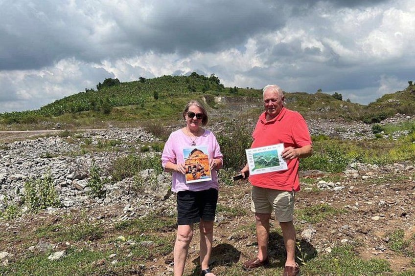 Two people standing on a rocky terrain with a hilly landscape in the background. 2