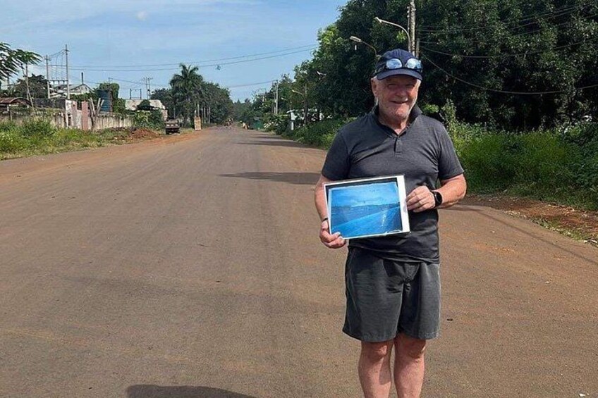 A man holding a framed picture on a rural road. 3