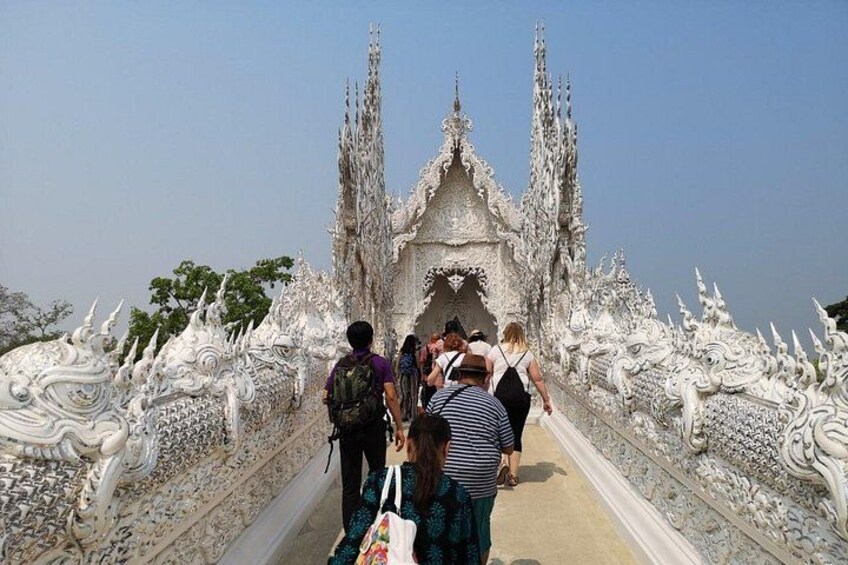 A white ornate structure with intricate carvings, a pathway leading to it, and a clear blue sky. 1