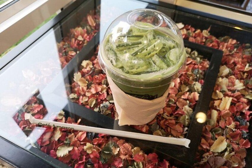 A green beverage in a clear cup with a straw, placed on a table with scattered flower petals. 4