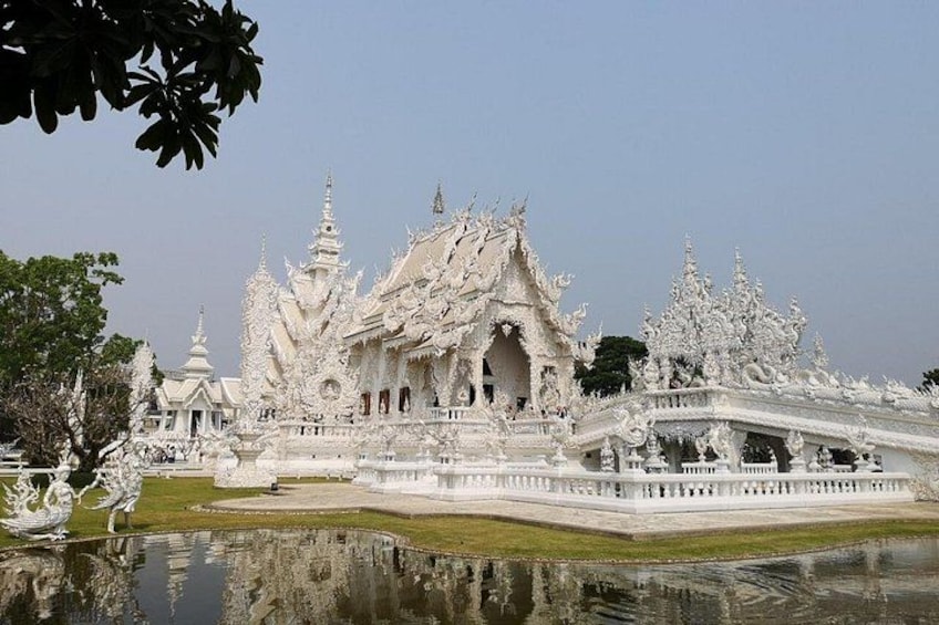 A white ornate temple with multiple spires and a reflection in the water. 2
