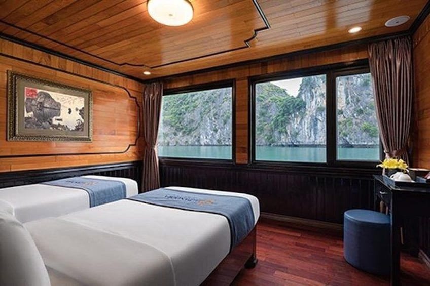 A cabin with wooden walls, two beds, a desk, and a window overlooking a body of water. 4
