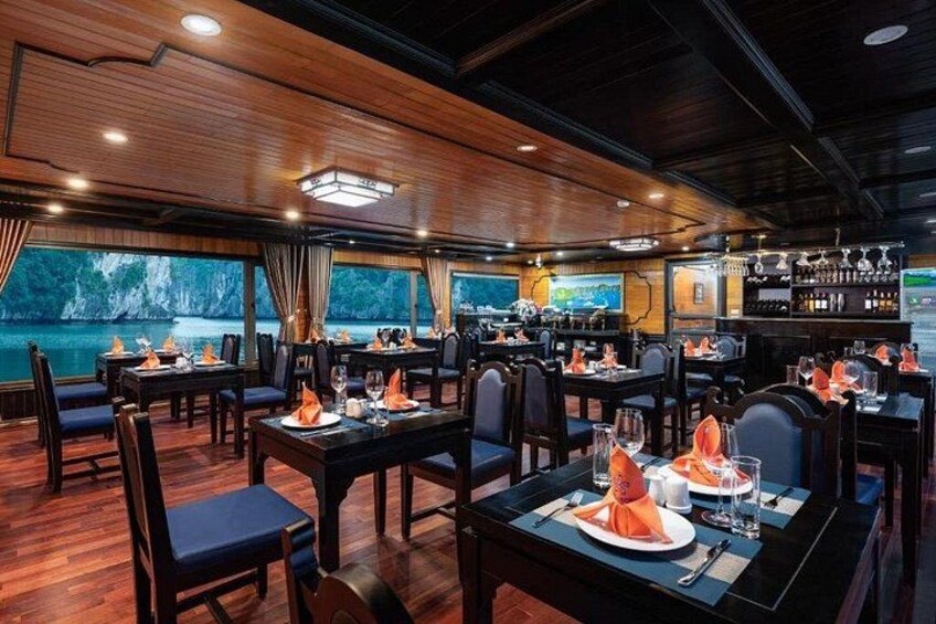 A restaurant with wooden interiors, tables set with orange napkins, and a view of a body of water. 3