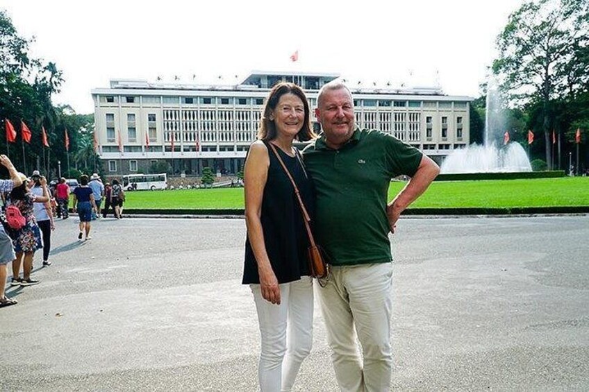 A man and woman standing in front of a building with a fountain in the background. 2