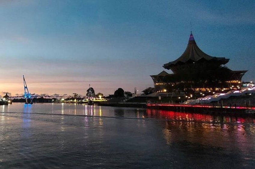 A traditional building with a distinctive roof, a body of water reflecting lights, and a bridge in the background. 3