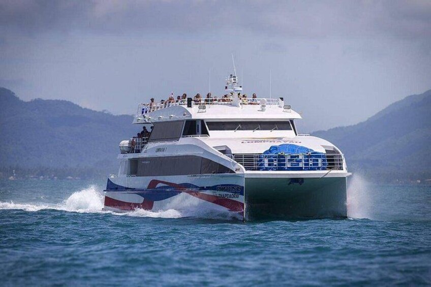 A large, multi-deck boat with passengers on the upper deck, moving through a body of water with mountains in the background. 2