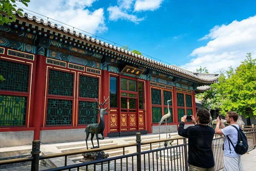 A traditional building with red walls and green window grills, a deer statue in front, and visitors taking photos. 2