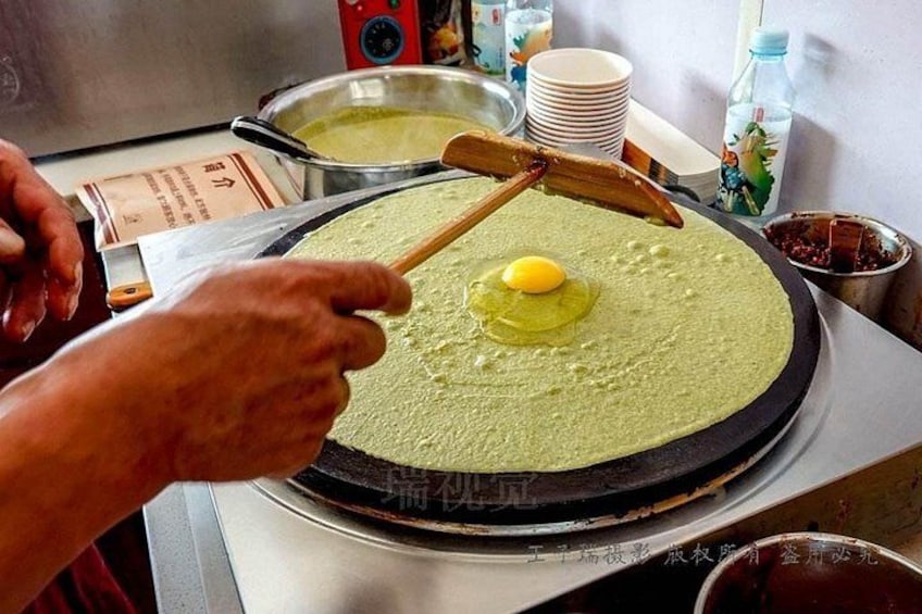 Una persona cucina su una ampia piastra di metallo, usando una spatola di legno mentre cuoce un uovo giallo. 5