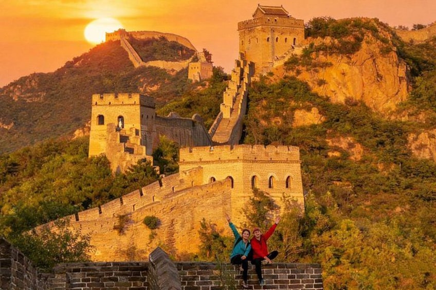 The Great Wall of China with two people standing on the wall, the sun setting in the background, and the surrounding landscape. 1