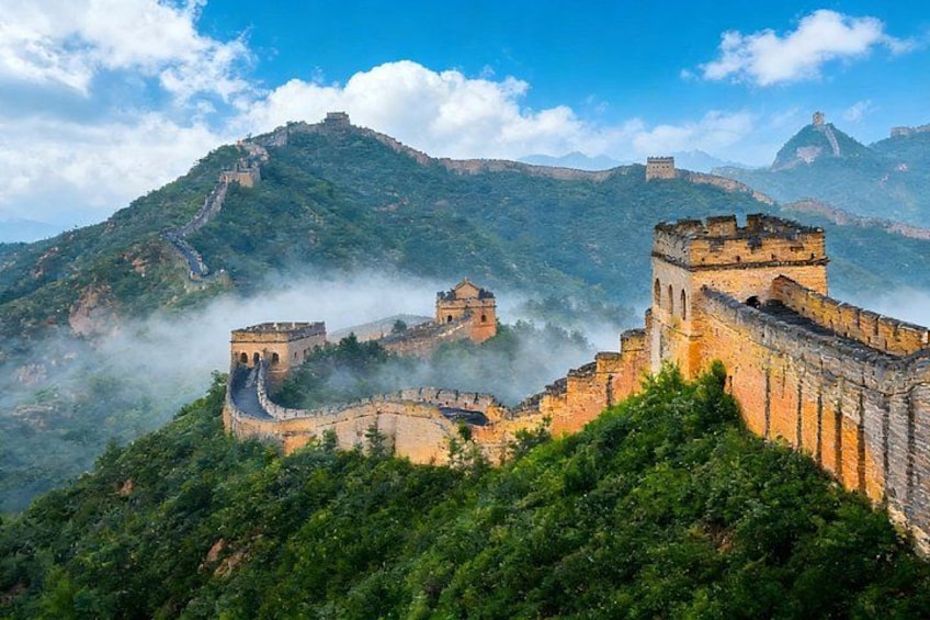 The Great Wall of China, a historic fortification, with lush green vegetation and mist-covered mountains in the background. 3