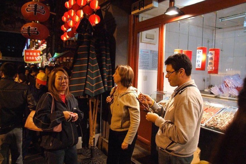 A street market with people shopping and a display case with items. 3