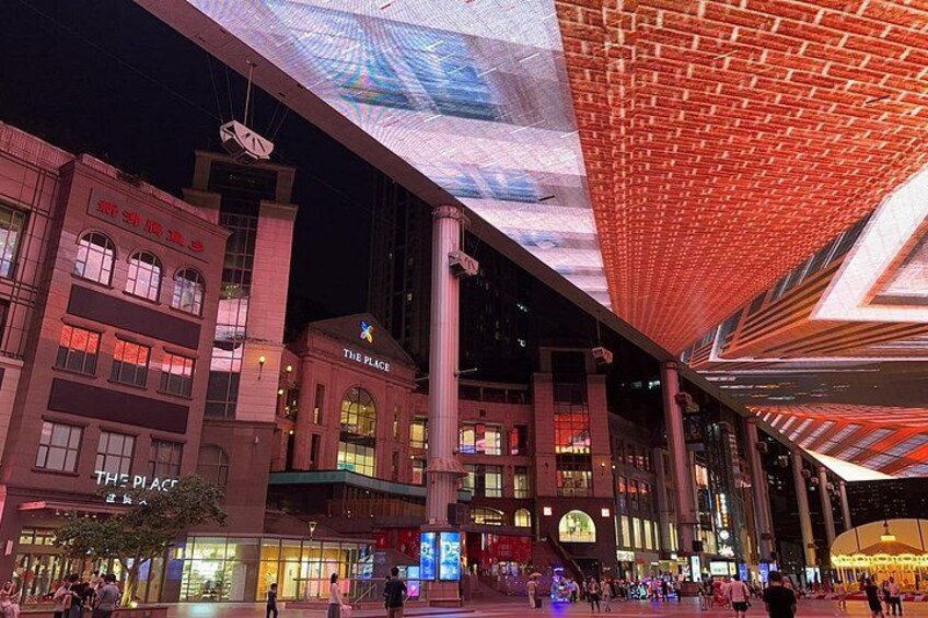 A brightly lit building with a large digital display on the facade and a sign that reads 'THE PLACE.' 2