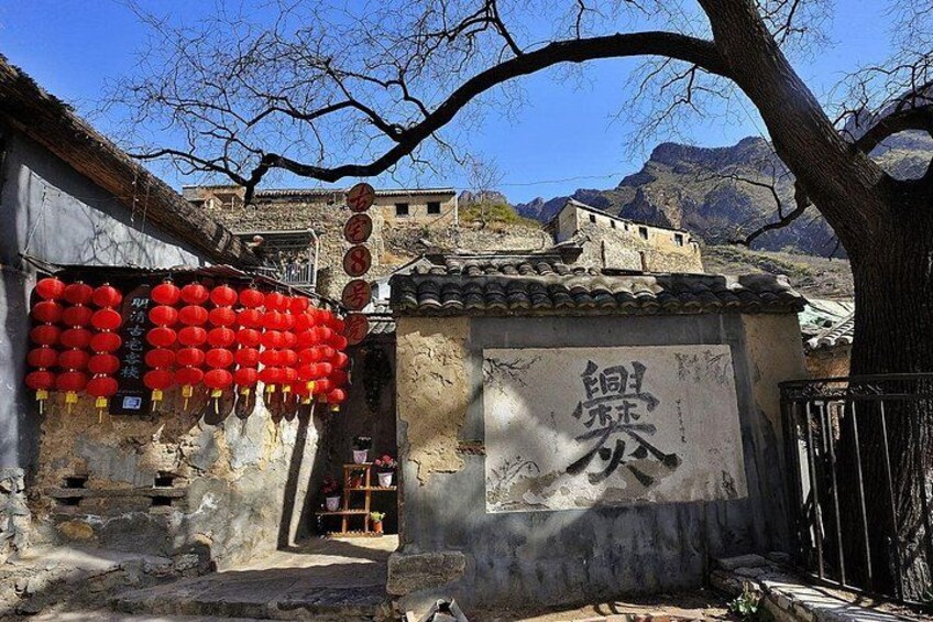 A traditional Chinese village with red lanterns, a stone gate with Chinese characters, and mountainous background. 5
