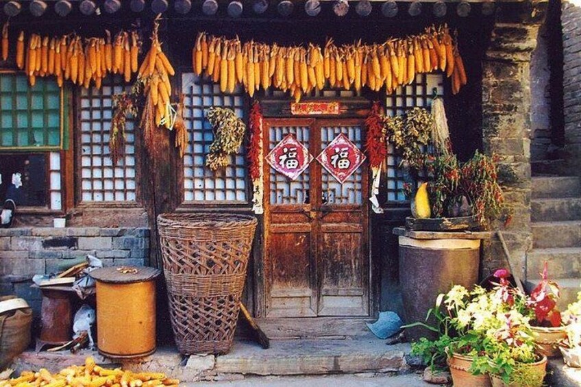 A traditional building with a wooden door, hanging bunches of bananas, and potted plants. 2