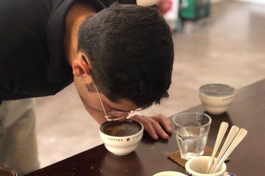Una persona beve caffè da una tazza con l'etichetta 'COFFEE', con un cucchiaino e un bicchiere d'acqua su un tavolo. 2