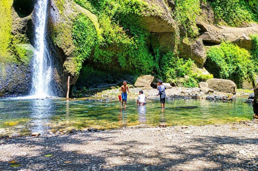 Una cascada, agua cristalina, terreno rocoso y gente de pie junto al agua. 3
