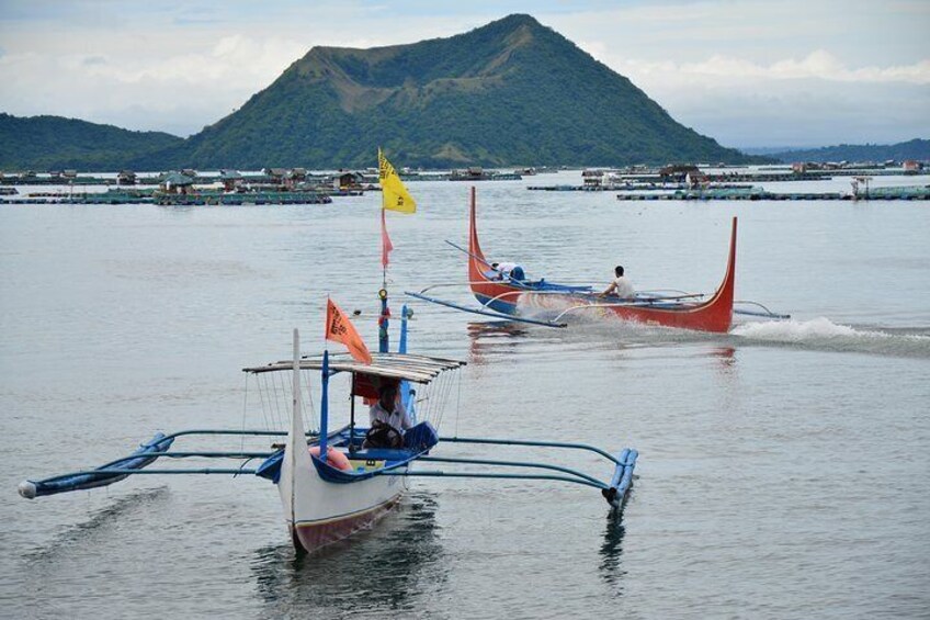 Des bateaux traditionnels dotés de balanciers sur une étendue d’eau calme, une montagne en arrière-plan et un ciel dégagé. 1