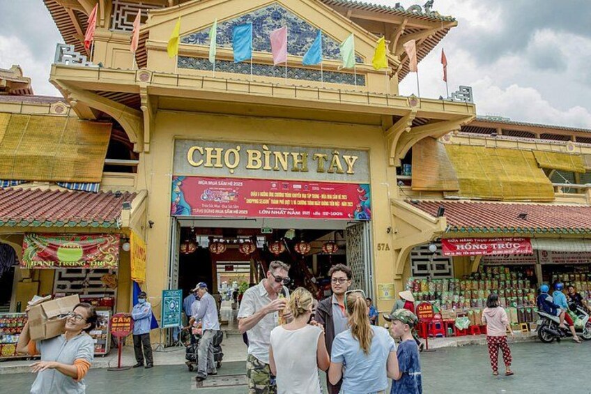 L'ingresso di un mercato tradizionale, con un cartello che riporta 'CHO BINTAY' e diversi negozi e bancarelle. 3