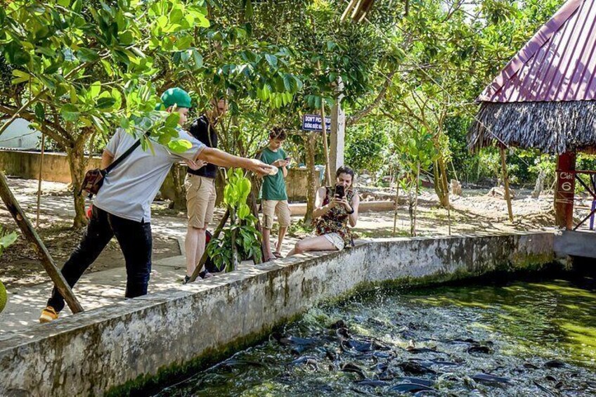 Un grupo de personas cerca de un cuerpo de agua, algunas de pie y otras sentadas, con una estructura de techo de paja al fondo. 5