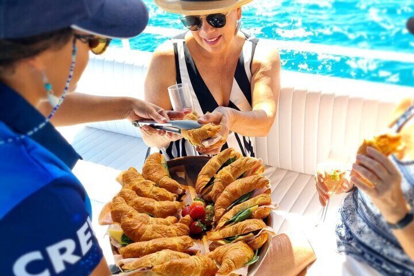 Eine Gruppe von Menschen genießt eine Mahlzeit am Pool mit Croissants und Sandwiches. 4