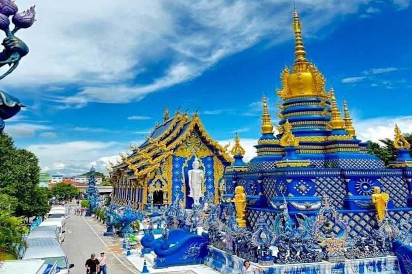 A temple with blue and gold architecture, a large statue, and a clear blue sky. 1