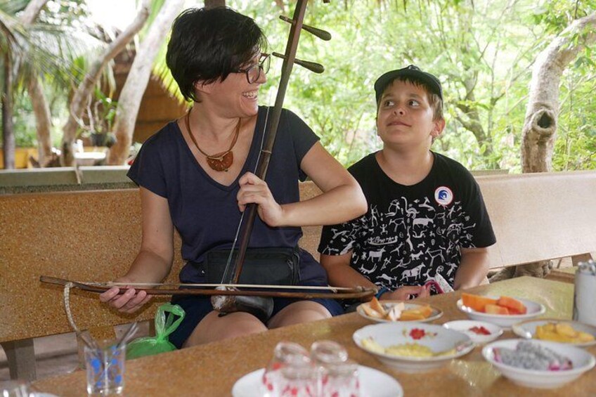 A person playing a stringed instrument, seated at a table with food and drinks. 3