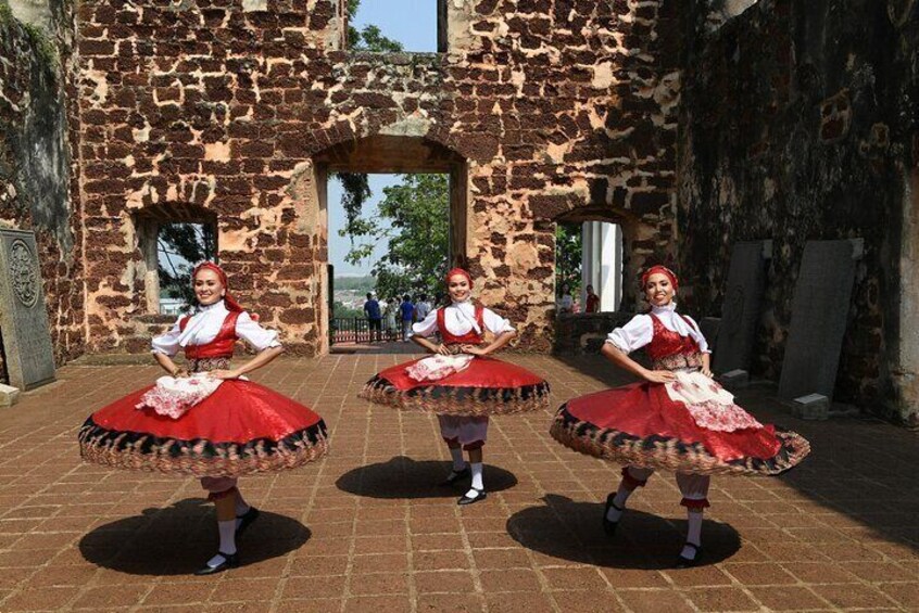 Three women in traditional red and white dresses dancing in front of a stone building. 4